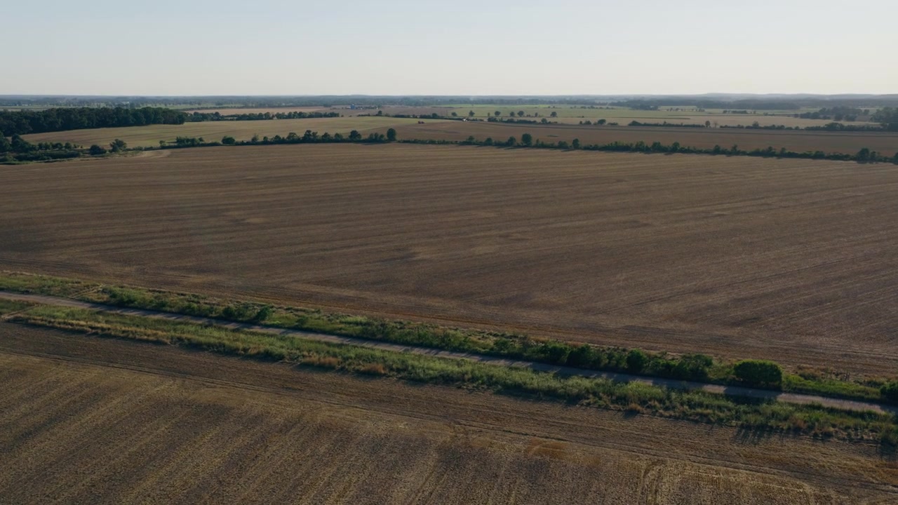 Luftfoto fanger vidstrakt tørt innhøstet jordbruksland avgrenset av grønne hekker og fjerne trerekker under en klar himmel