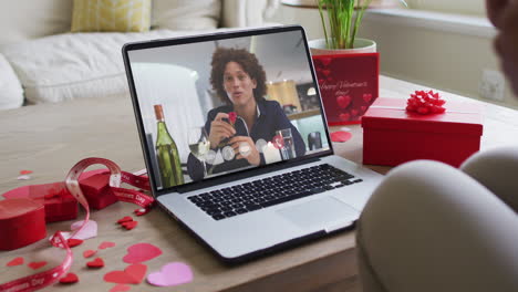 happy biracial man with wine making valentine's day video call on laptop