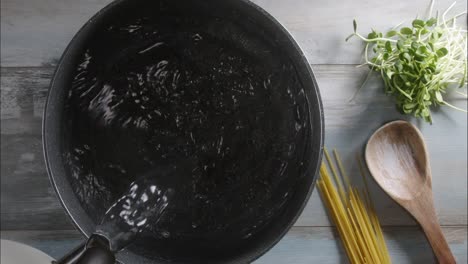 overhead shot: pouring water in a pot before starting to cook spaghetti pasta