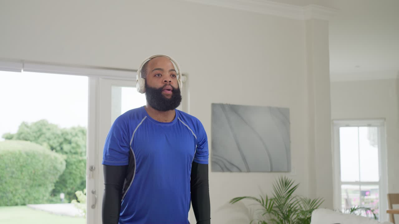 African American man taking breath lifting hex weights at home wearing headphones building strength