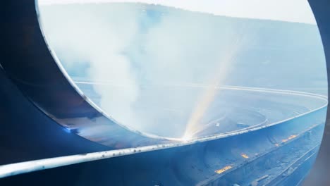 un primer plano del proceso de soldadura industrial dentro de una gran estructura metálica curva. chispas volando y humo subiendo mientras el trabajador suela el metal