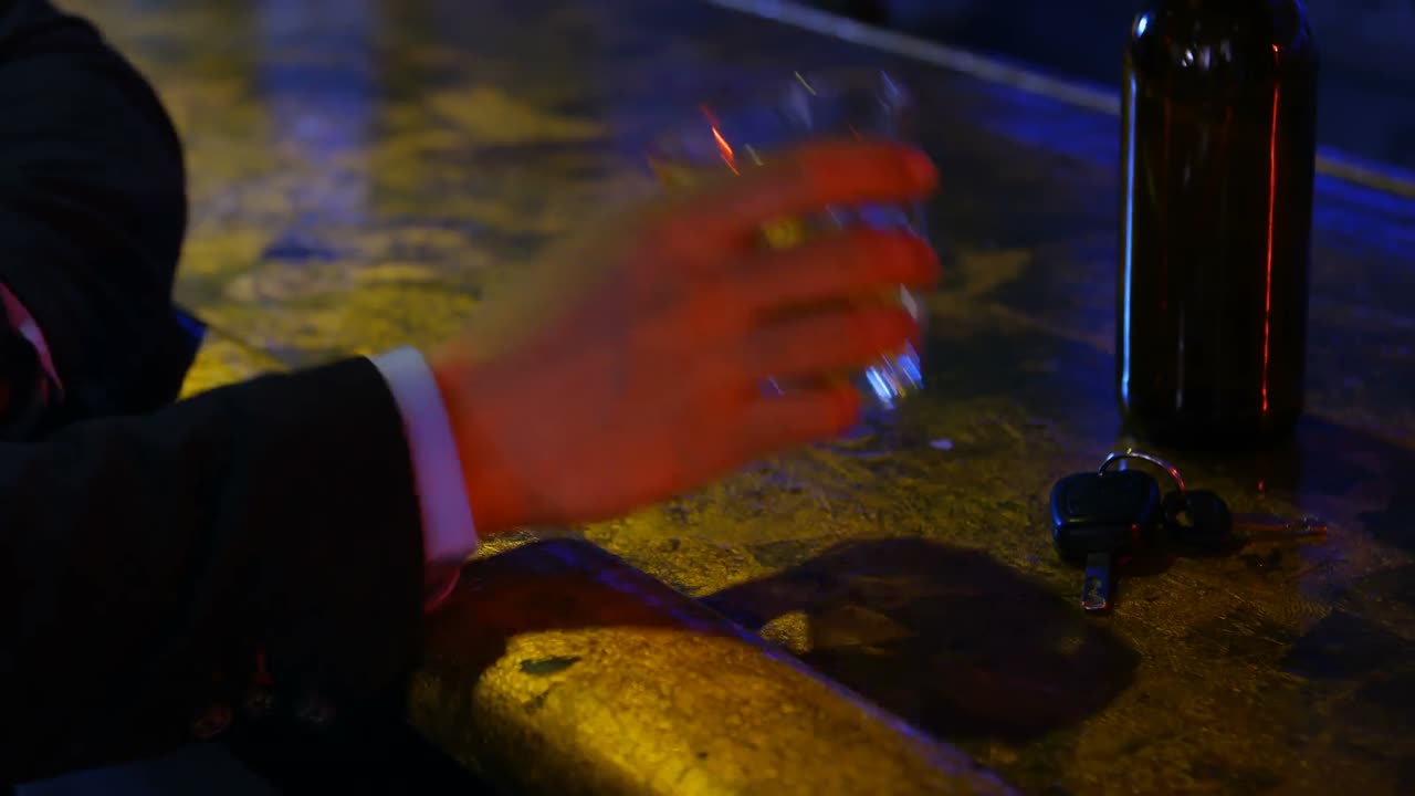Mano che prende un bicchiere di whisky al bancone