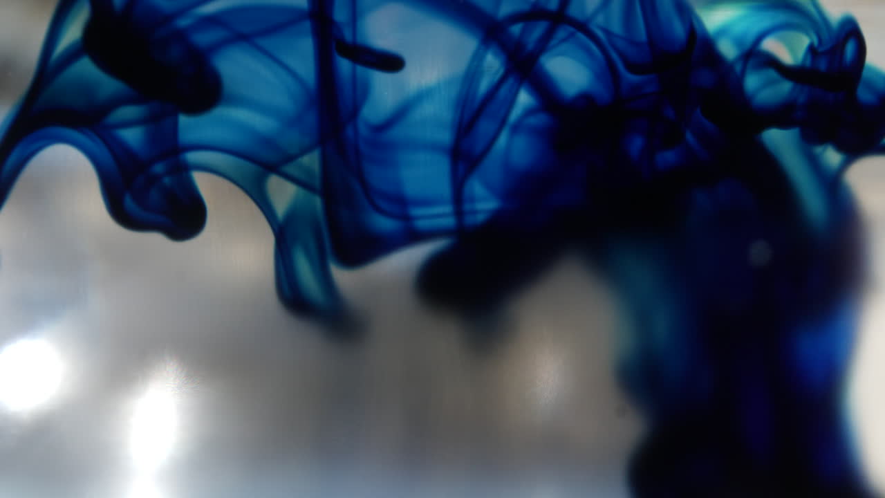 Macro shot of a blue ink drop in clear water as it spreads out underwater and creates smokey abstract shapes in the background