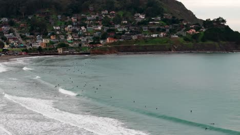 Stationäre-Drohnenaufnahme-Vieler-Surfer,-Die-An-Einem-Bewölkten-Tag-Die-Großen-Wellen-Genießen