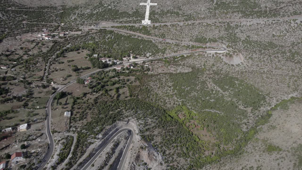 알바니아 브리제에 있는 sh20 도로의 산길 시작 부분에 대한 설명적인 패닝의 드론 비디오, 우리는 종교적 흰색 십자가, 마을의 집들을 볼 수 있고, 구불구불한 길을 볼 수 있습니다.