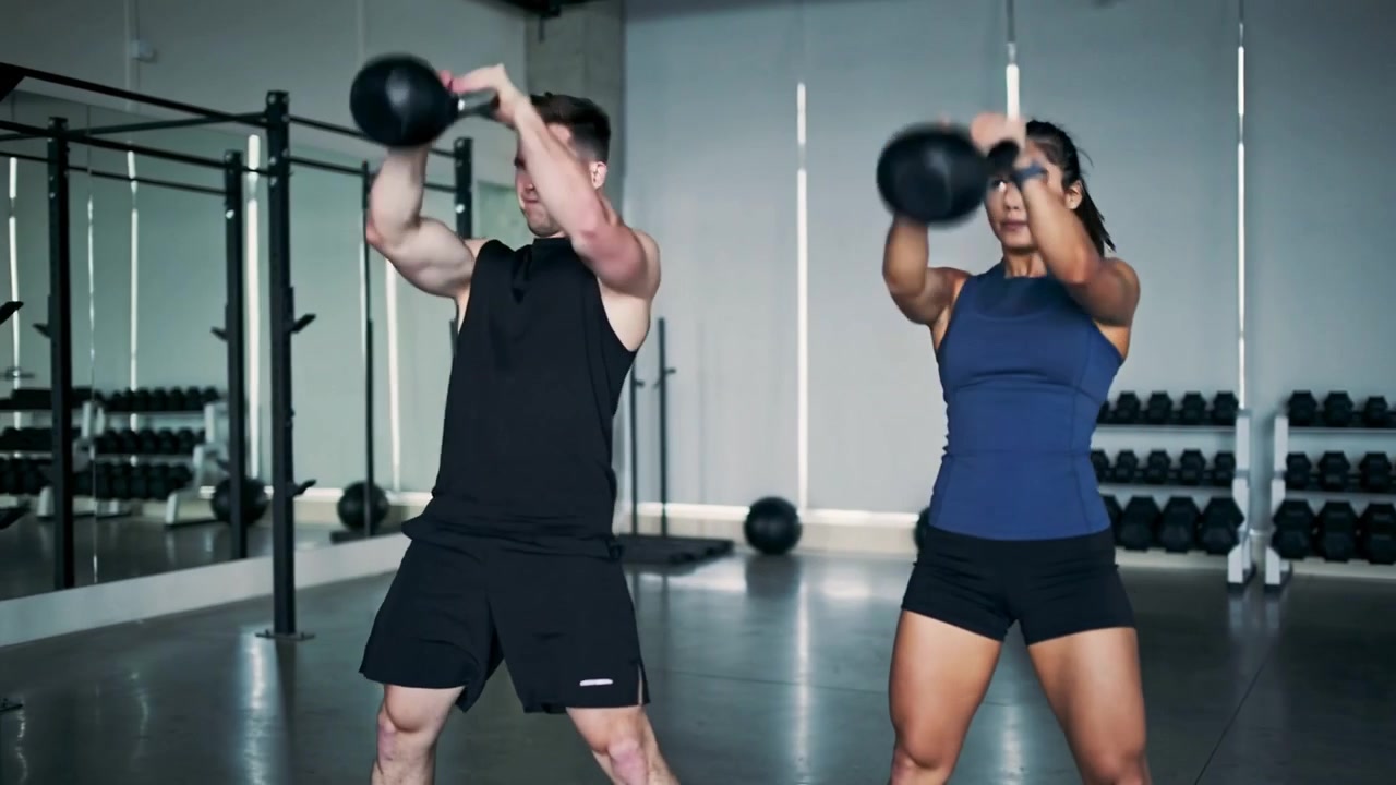 Partendo dalla cerniera dell'anca, due partner eseguono swing con kettlebell in palestra in pantaloncini per la forza.