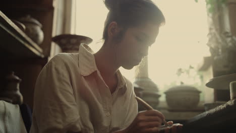 focused girl decorating plate in studio. woman working with wet clay in pottery