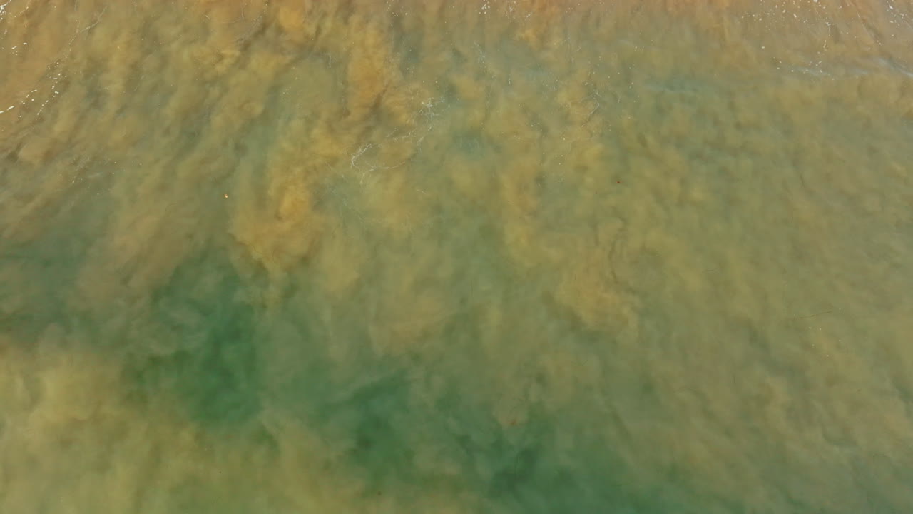 Le onde vanno e vengono dalla spiaggia sabbiosa. Prospettiva aerea sulla marea dell'Oceano Pacifico.
