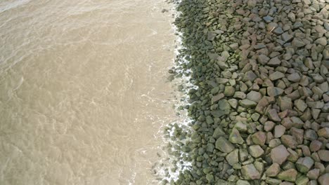 Olas-Del-Mar-Golpeando-Rocas-En-Un-Dique-Marino,-Drones-Volando-Hacia-Atrás