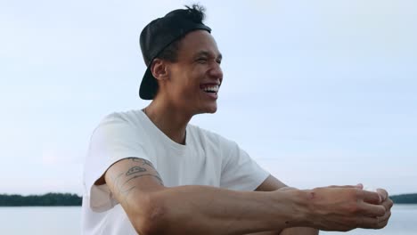 cinematic video of a young and happy man breaking into a laugh after hearing a funny jake whilst standing on the waters edge near the ocean