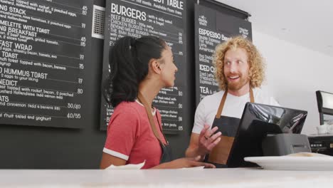 happy diverse male and female baristas wearing aprons talking behind the coiunter in cafe