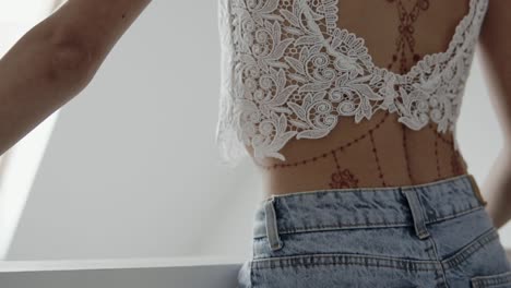 mujer con una camiseta blanca recortada y vaqueros de vaqueros con tatuaje de henna en la espalda