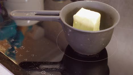 butter is tossed into small pot on induction stove to melt, closeup