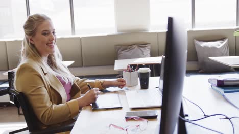 Happy-caucasian-casual-businesswoman-in-wheelchair-using-tablet-in-office,-in-slow-motion