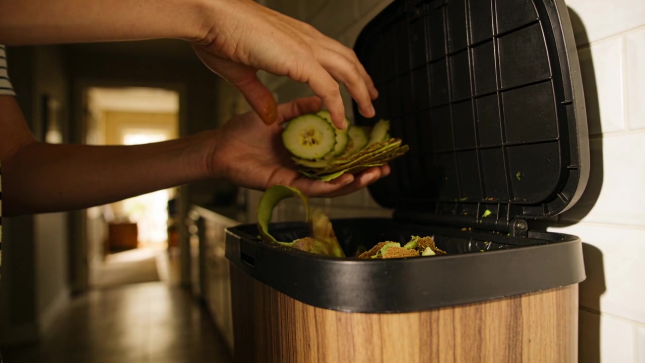 Finishing peeling, hands in striped shirt placing green slices and peels into kitchen compost bin