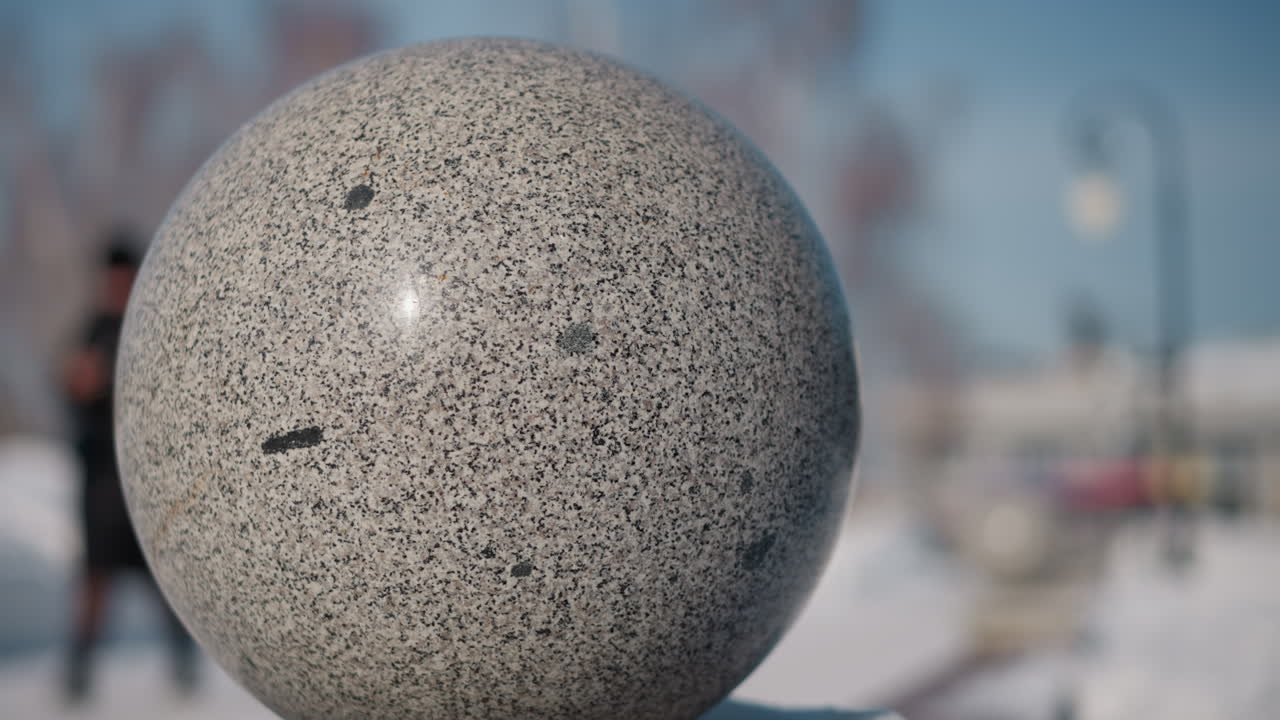 Orbicular on snow covered pedestal with blurred snowy park background under crisp winter daylight showcasing textured stone surface and focus winter environment