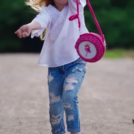 happy child is running in summertime. beautiful little girl in stylish jeans holds pink handbag and runs joyfully outdoors in summer.