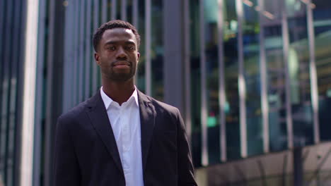 Portrait-Of-Confident-Young-Businessman-Wearing-Suit-Folding-Arms-Standing-Outside-Modern-Offices-In-The-Financial-District-Of-The-City-Of-London-UK