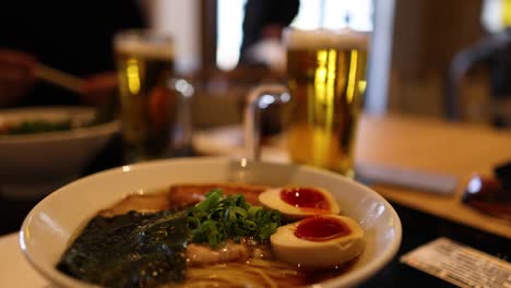 close-up of ramen bowl with beer in background