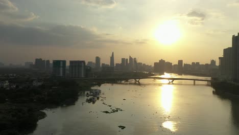 tracking across the saigon river, vietnam from drone with view to bridge and modern city skyline at sunset