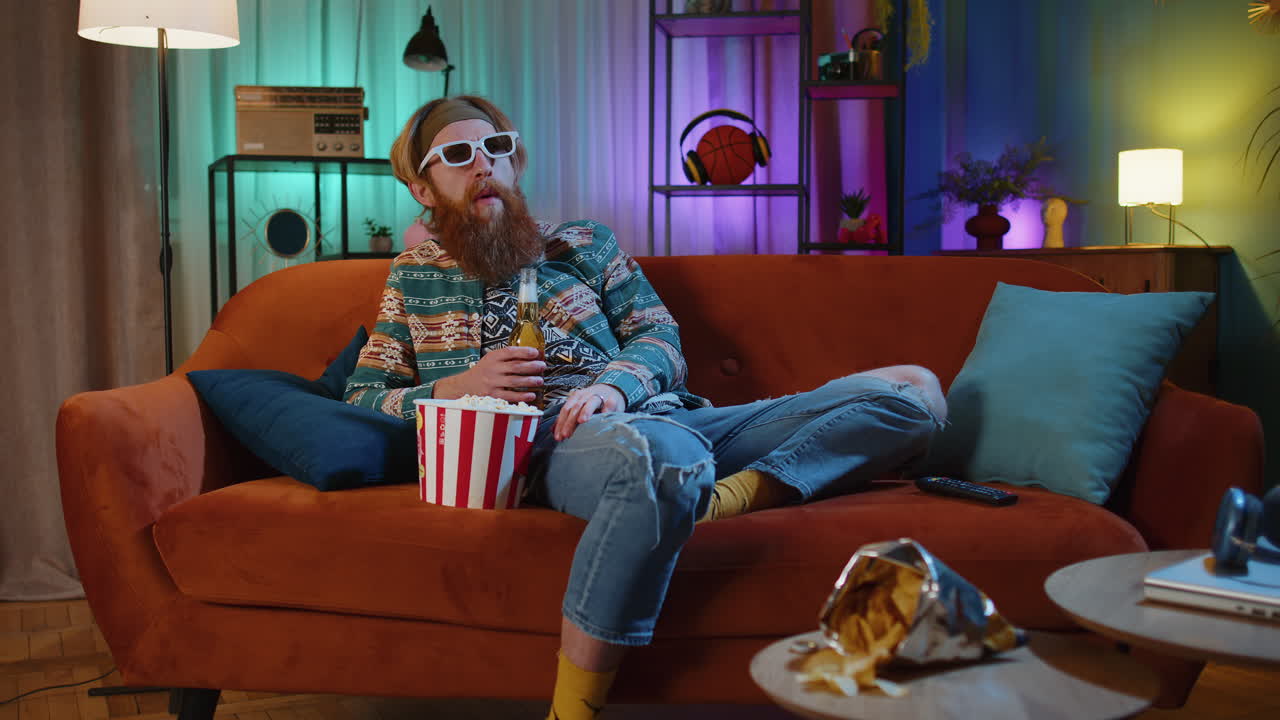 человек смотрит телевизор на диване с попкорном и пивом