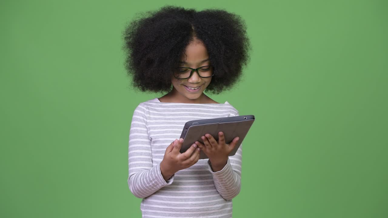 Young cute African girl with Afro hair using digital tablet