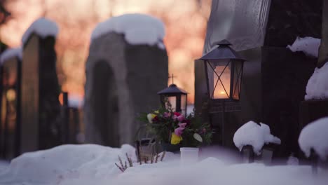 candle inside a lantern in front of a snowy grave at dusk