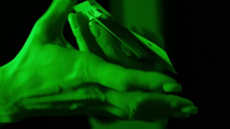 green-lit hands shuffle playing cards, close-up scene filled with mystery, focus