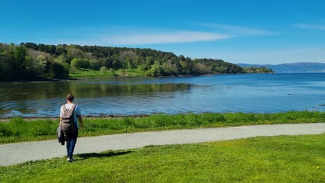 a young man strolls along the shoreline in lade by a norwegian fjord on a sunny spring day, enjoying the stunning landscape and clear blue sk