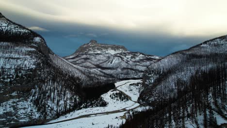 Vista-Aérea-Escénica-De-Drones-Del-Valle-Natural-Cubierto-De-Nieve-En-La-Montaña-Rocosa