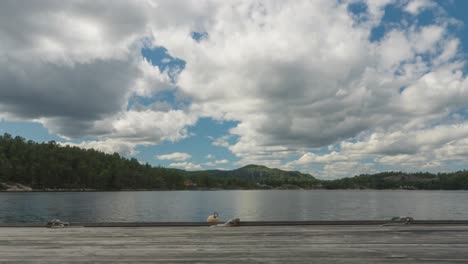 Time-lapse-of-clouds-forming-over-lake-wooden-pier-decking,-zoom-view