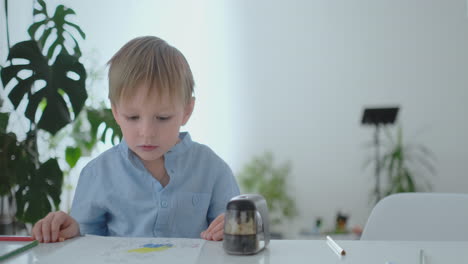 A-small-child-sitting-at-the-table-draws-a-pencil-drawing-painting-in-different-colors