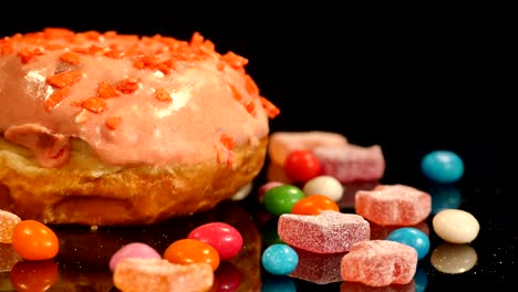 orange funny surprised glazed donut with sprinkles, striped caramel candies, colorful dragee with raisins or peanuts inside rotate on black background