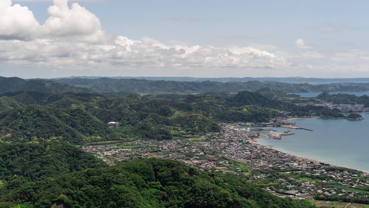 Cảnh quay timelapse toàn cảnh rộng trên một thị trấn biển nhỏ với những ngọn đồi thoai thoải, đại dương và những đám mây - Cảnh quay đẩy vào.