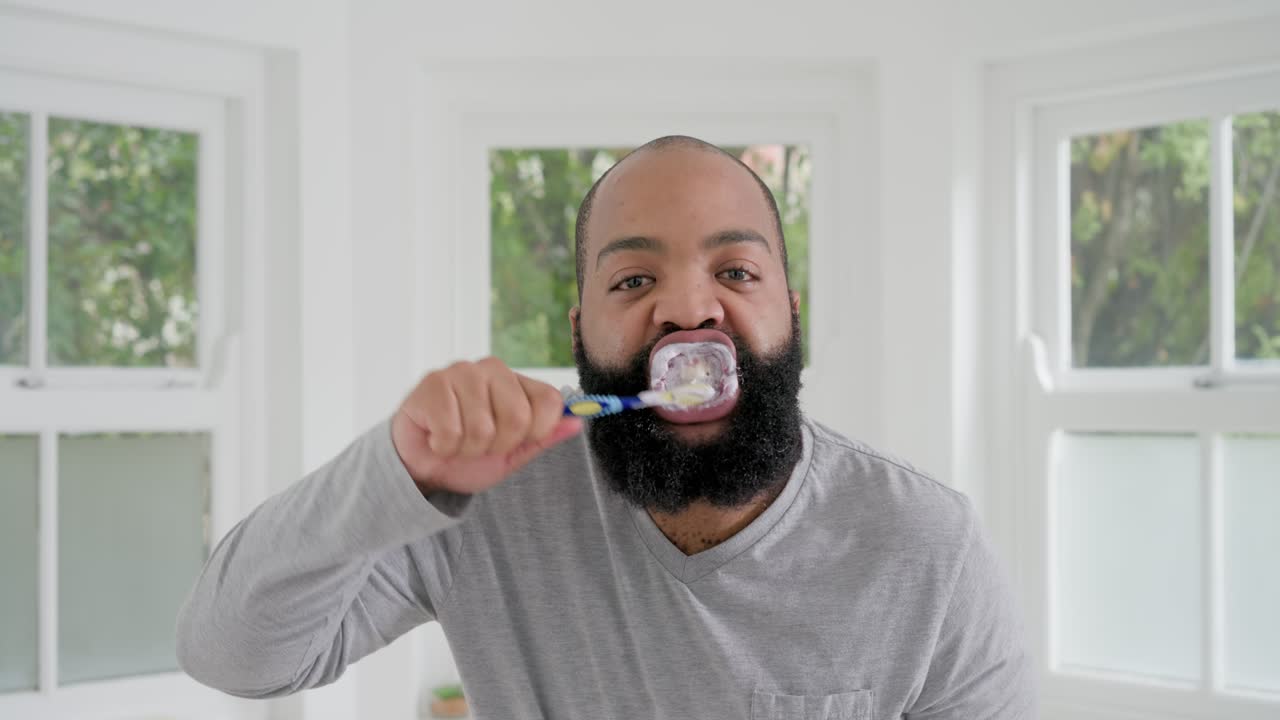 African American man bringing blue brush to mouth at home, brushing foamy teeth for oral care