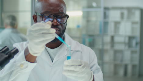 african american lab scientist pouring blue liquid chemical in test tube