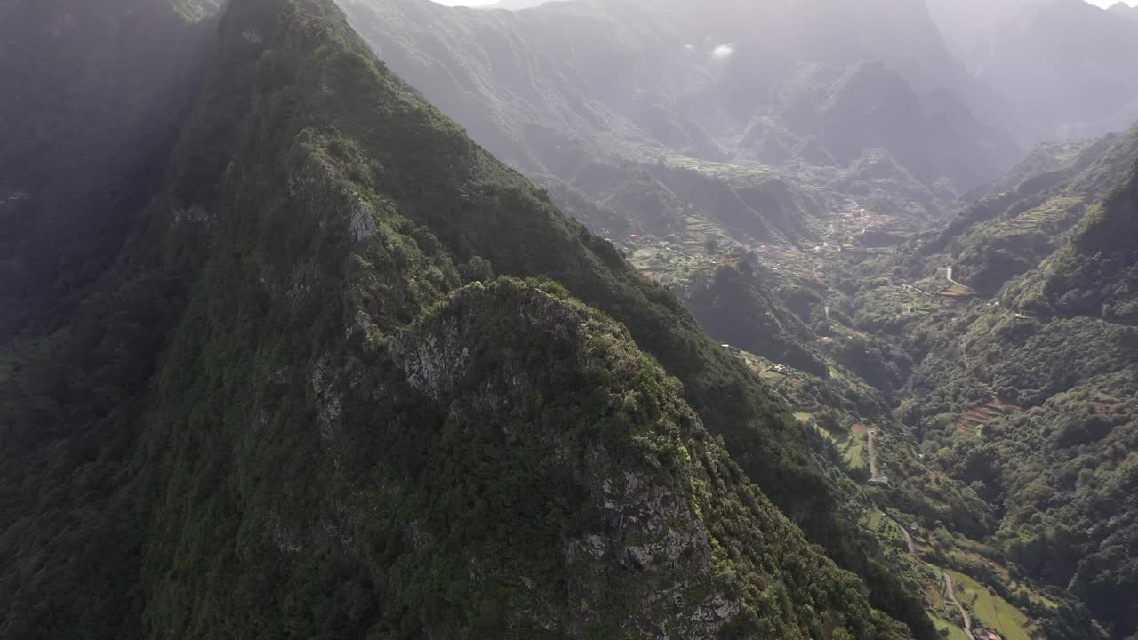 disparo de drones en círculos, centrándose en la cresta de una montaña con dos lados con casas de pueblos en madeira