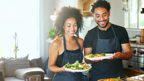 a man and woman in a kitchen holding plates of food