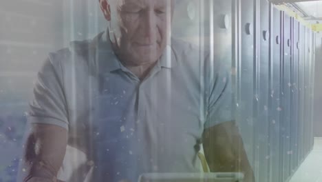 Animation-of-white-particles-over-caucasian-senior-man-using-digital-tablet-against-server-room