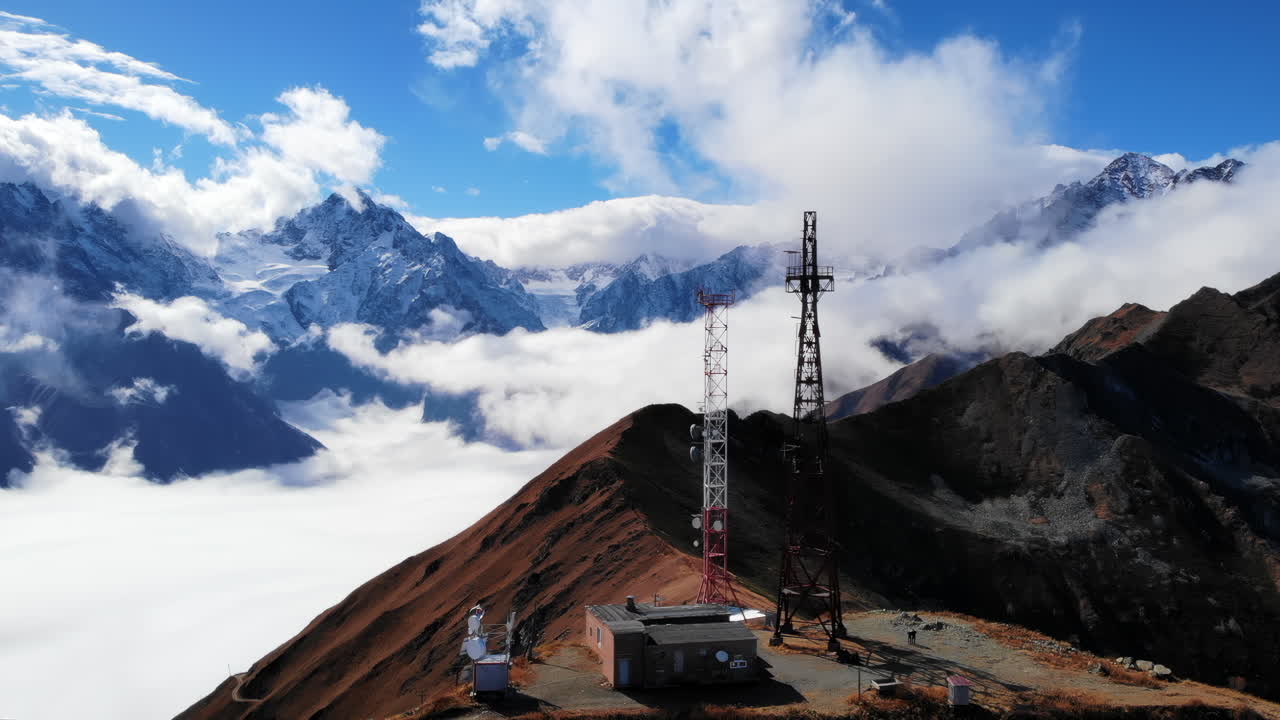 Torre di comunicazione su crinale avvolto dalle nuvole, capanne rustiche per attrezzature e antenne appollaiate sopra un mare di nebbia