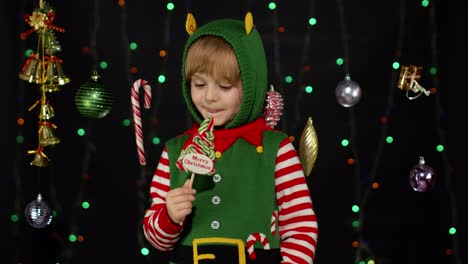 Kid-girl-in-Christmas-elf-Santa-Claus-helper-costume-licking-candy-lollipop-caramel-sweets