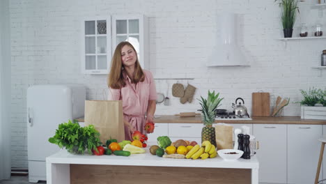 Happy young woman with fresh apples in the kitchen. Beautiful housewife holds and sniffs natural fruit on the background of healthy food on the table. Vertical video