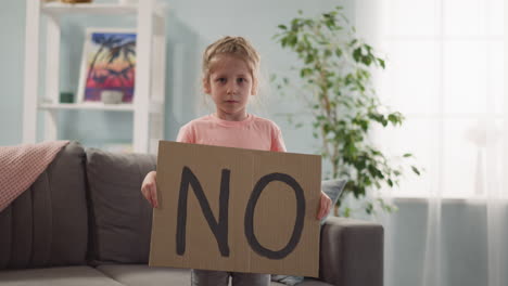 una niña cansada, triste y resentida se pone de pie y sostiene un cartel