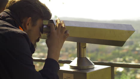 male viewing city from the top point through public binoculars