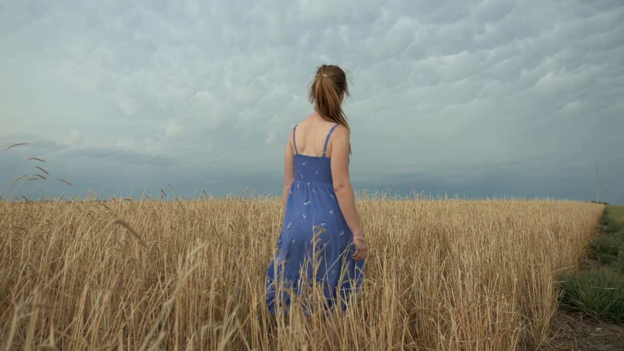 Woman walking in a wheat field under a cloudy sky