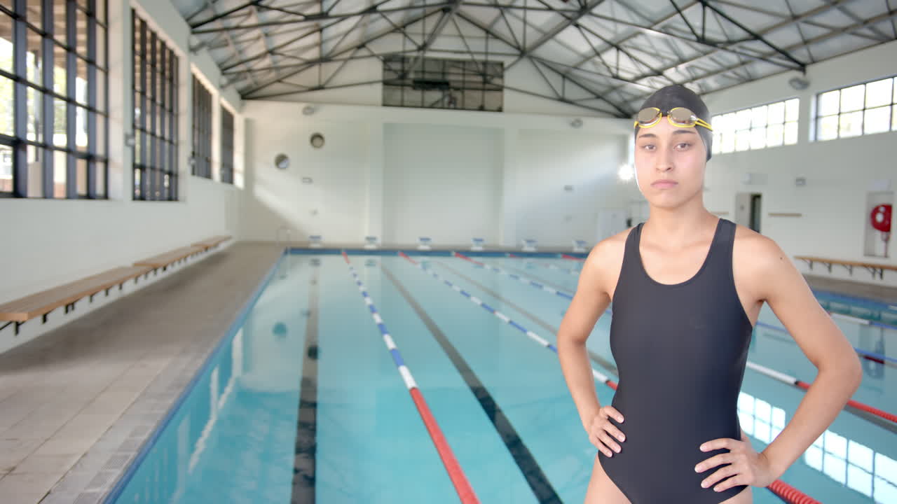 Female Swimmer in swimsuit and goggles standing confidently by indoor pool, copy space