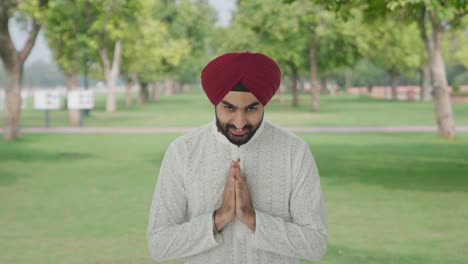 happy sikh indian man doing namaste in park