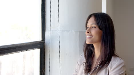smiling businesswoman looking out window, taking break from work in office, copy space