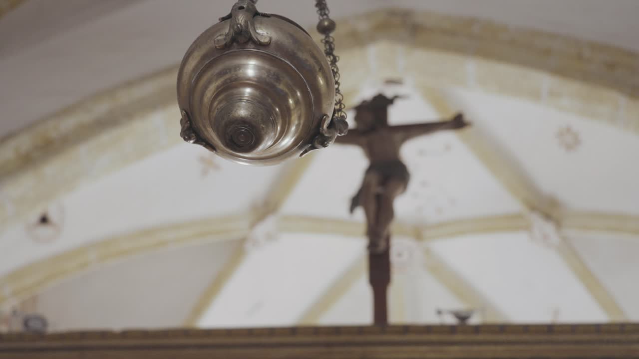 кинематографический отслеживающий кадр начинается с фокуса на кадильнике, затем смещает фокус на распятие на заднем плане