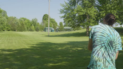 Un-Hombre-Demuestra-La-Técnica-De-Un-Lanzamiento-De-Disc-Golf-En-Un-Parque-Soleado,-Enfatizando-La-Forma-Y-La-Concentración-Requeridas-Para-El-Deporte